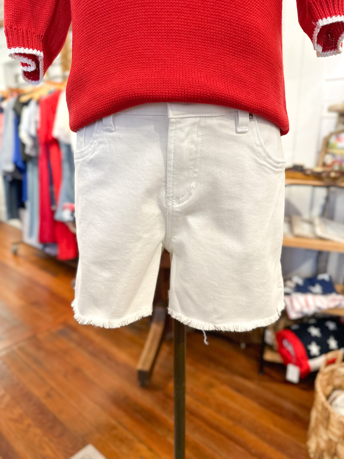 White shorts on a mannequin with a red sweater in a store setting dear john gigi shorts in white 