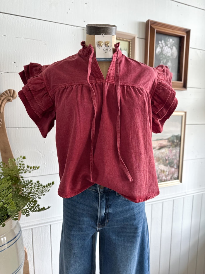 Red blouse with ruffled sleeves on a mannequin against a white wall with framed pictures.