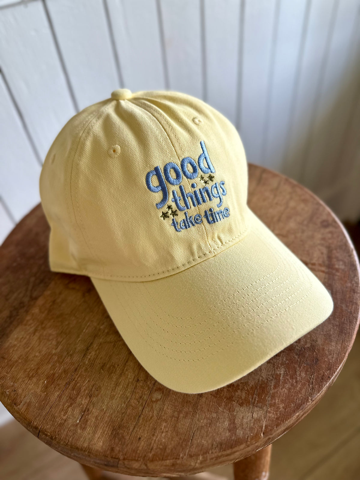 Yellow cap with 'good things take time' text on a wooden stool.