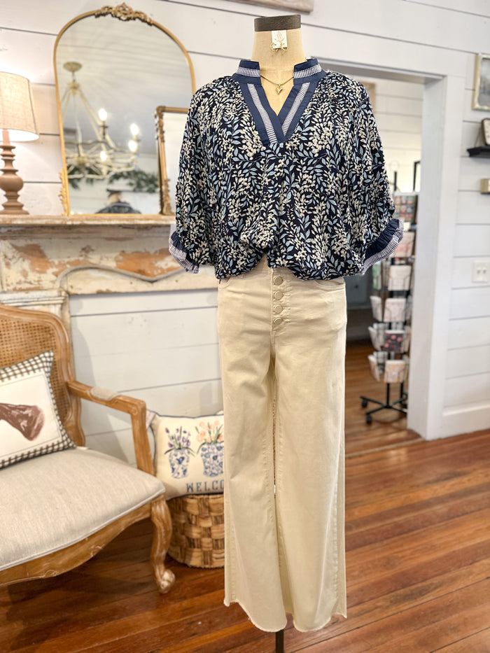 Mannequin wearing a patterned blouse and beige pants in a room with wooden floor and furniture.
