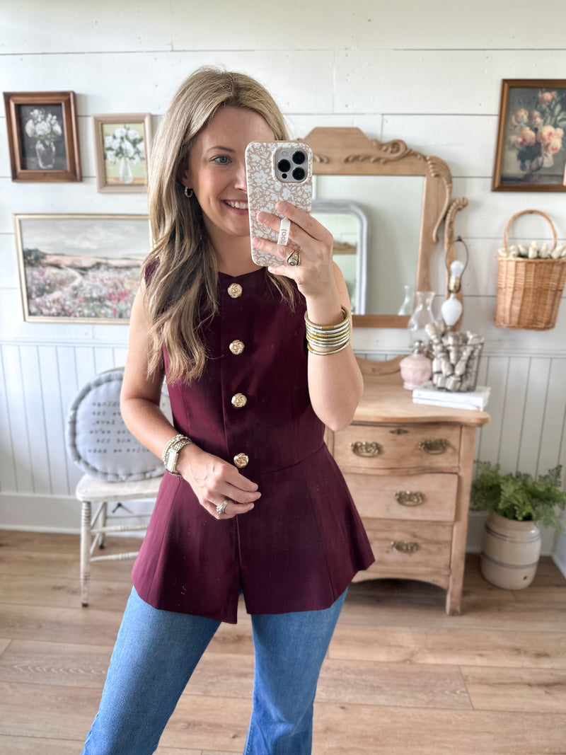 Woman taking a mirror selfie wearing a burgundy top and blue jeans in a room with wooden furniture and decor.