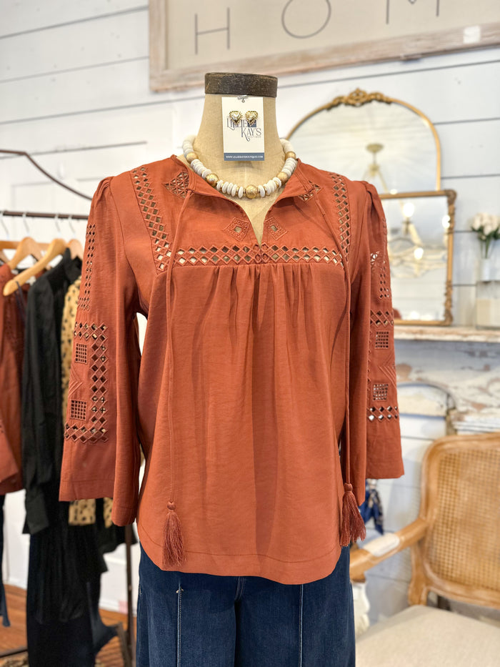 Brown blouse with intricate details on a mannequin in a store setting.