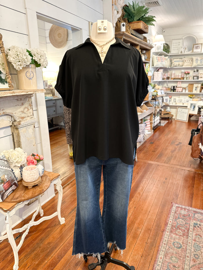 Mannequin wearing a black top and blue jeans in a store setting with wooden floors and shelves.