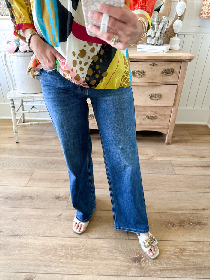 Person wearing a colorful top and blue jeans standing on a wooden floor. dark wash relaxed fit straight leg jean 