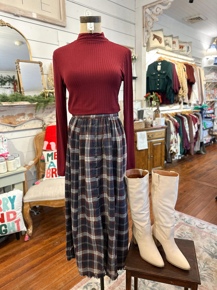 Mannequin wearing a red ribbed sweater, plaid skirt, and white boots in a store setting.