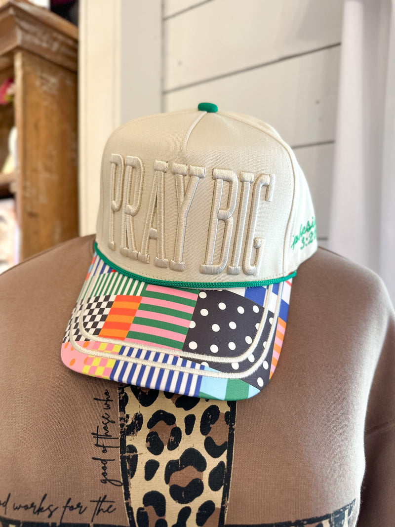 Colorful cap with 'PRAY BIG' text worn by a person