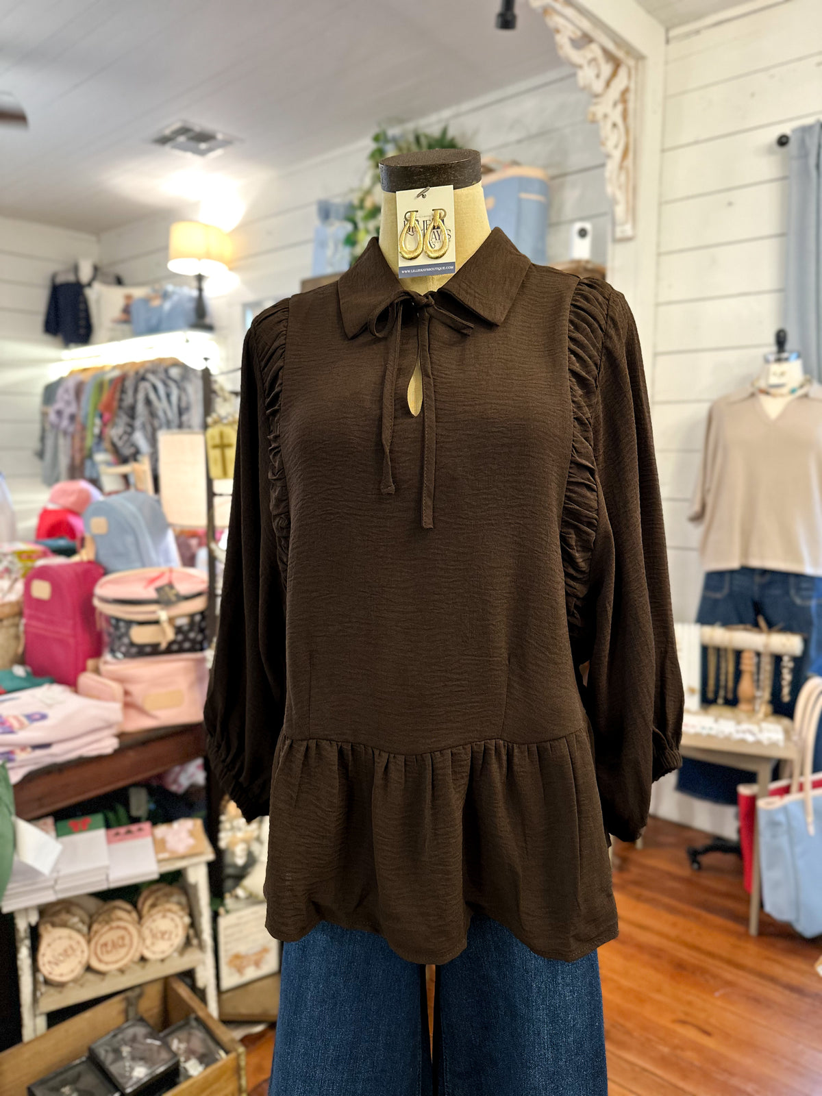 rich brown long sleeve blouse with collar and ruffle hem inside store setting 