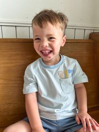 Child sitting on a wooden bench with a white wall background tool applique designs on shirt 