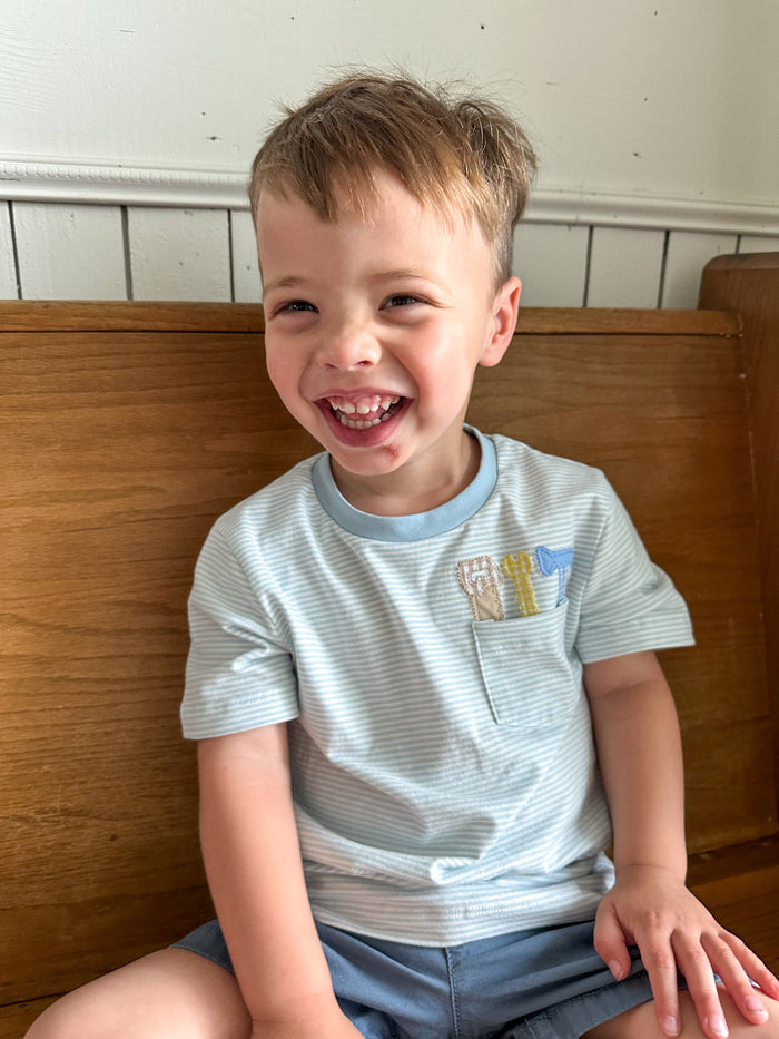 Child sitting on a wooden bench with a white wall background tool applique designs on shirt 