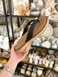 Hand holding a sandal with cork sole in front of decorative items