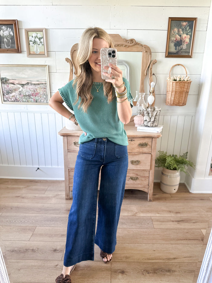 Woman taking a mirror selfie wearing a green sweater and blue jeans in a room with wooden flooring and white walls. jade color sweater top