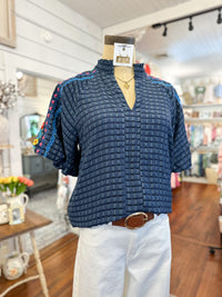Mannequin wearing a blue textured shirt with colorful trim in a store setting
