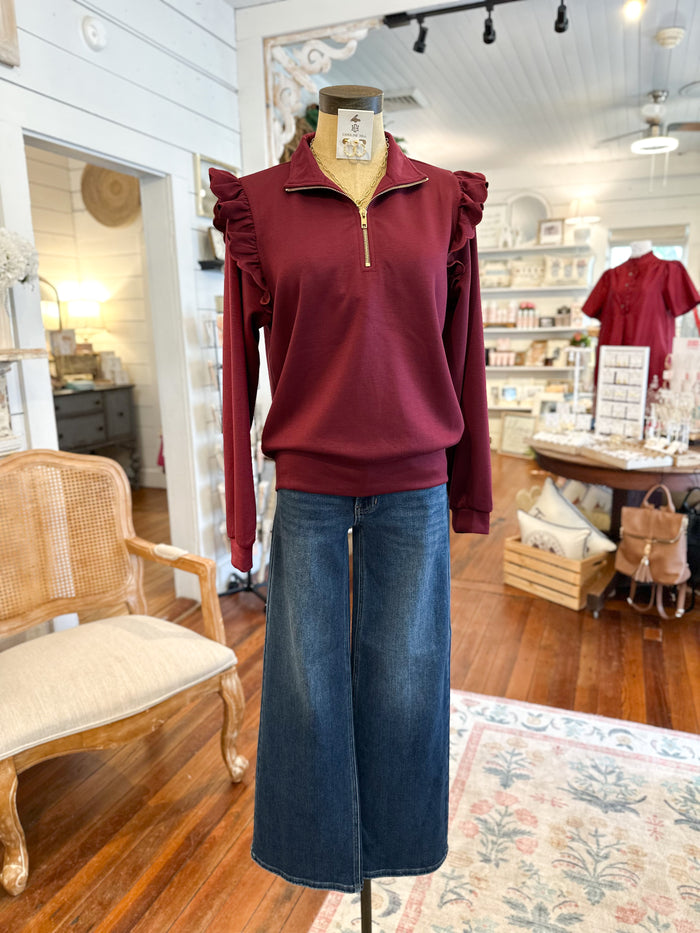 Mannequin wearing a burgundy sweater with ruffled shoulders and blue jeans in a store setting.