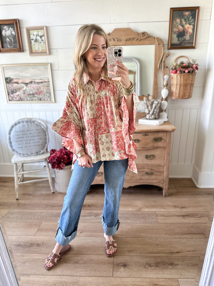 Woman taking a mirror selfie wearing a patterned blouse and jeans in a home setting.