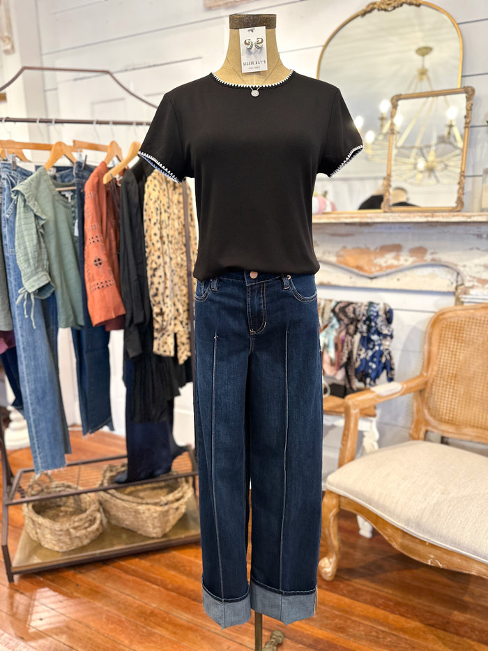 Mannequin wearing a black t-shirt and blue jeans in a store setting with clothing racks and a chair.