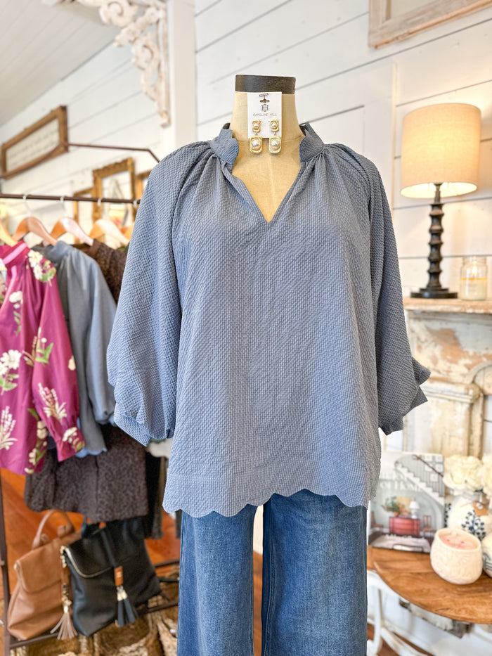 Mannequin wearing a blue textured top and jeans in a store setting with clothing racks and decor. umgee top blue scallop hem 