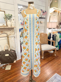 Patterned dress on a mannequin in a store setting with furniture and clothing in the background.