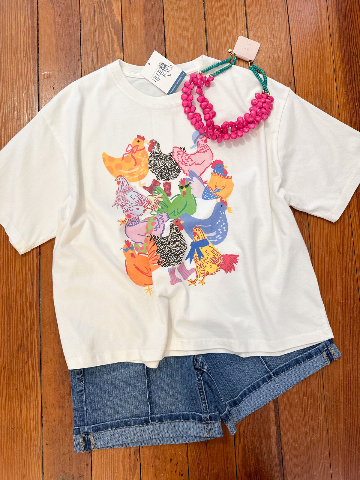 White t-shirt with colorful chicken 
graphic design on a wooden surface