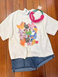 White t-shirt with colorful chicken 
graphic design on a wooden surface