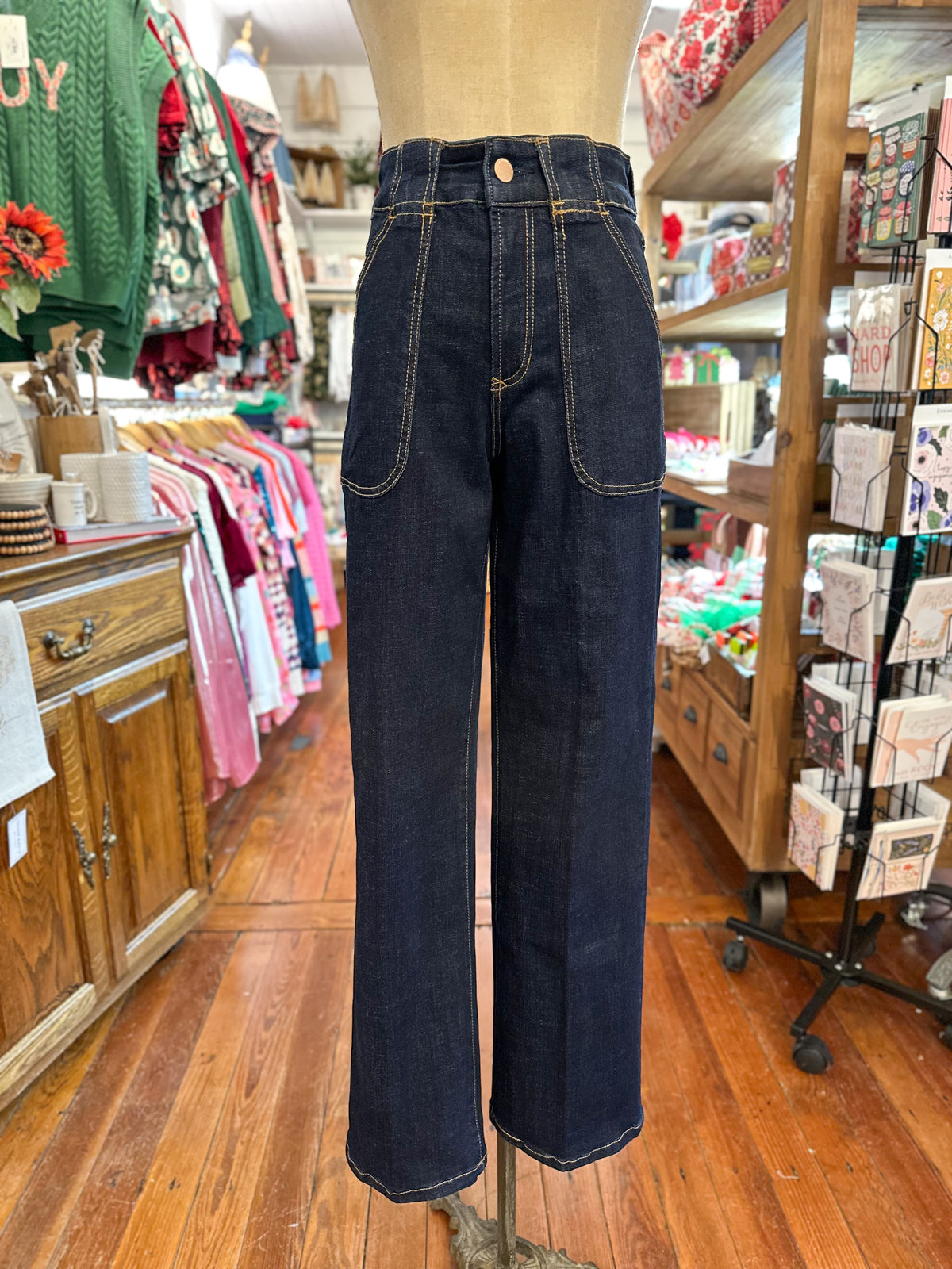 Dark blue jeans on a mannequin in a store setting with clothing racks and displays.