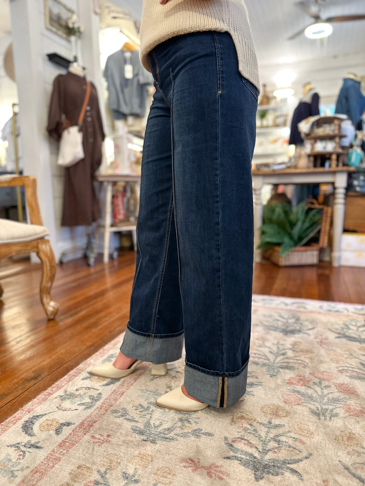 Person wearing dark blue jeans standing on a patterned rug in a store setting.