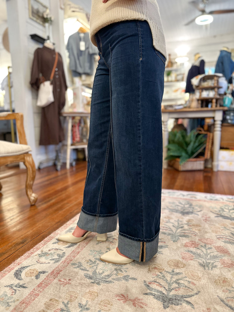Person wearing dark blue jeans standing on a patterned rug in a store setting.
