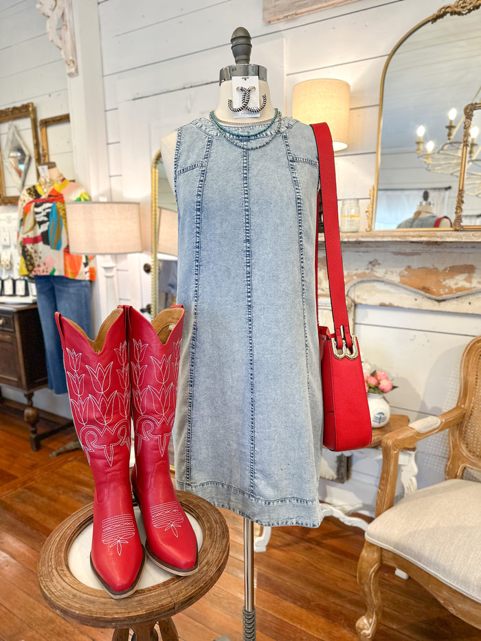 Mannequin wearing a denim dress with red cowboy boots and handbag in a store setting.