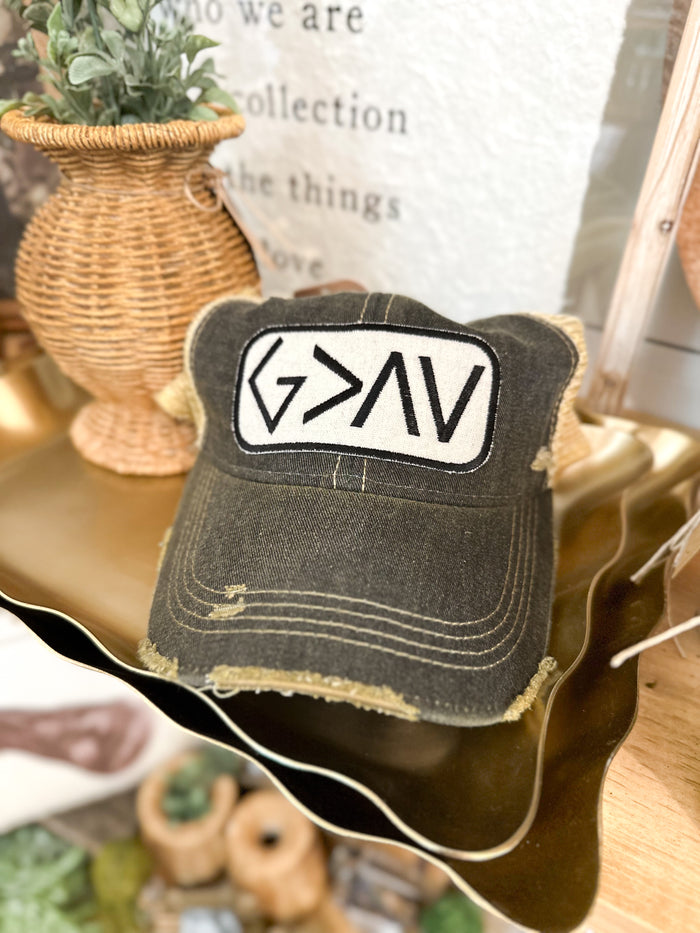 Black distressed cap with a white patch featuring god is greater than highs and lows symbols on a blurred background