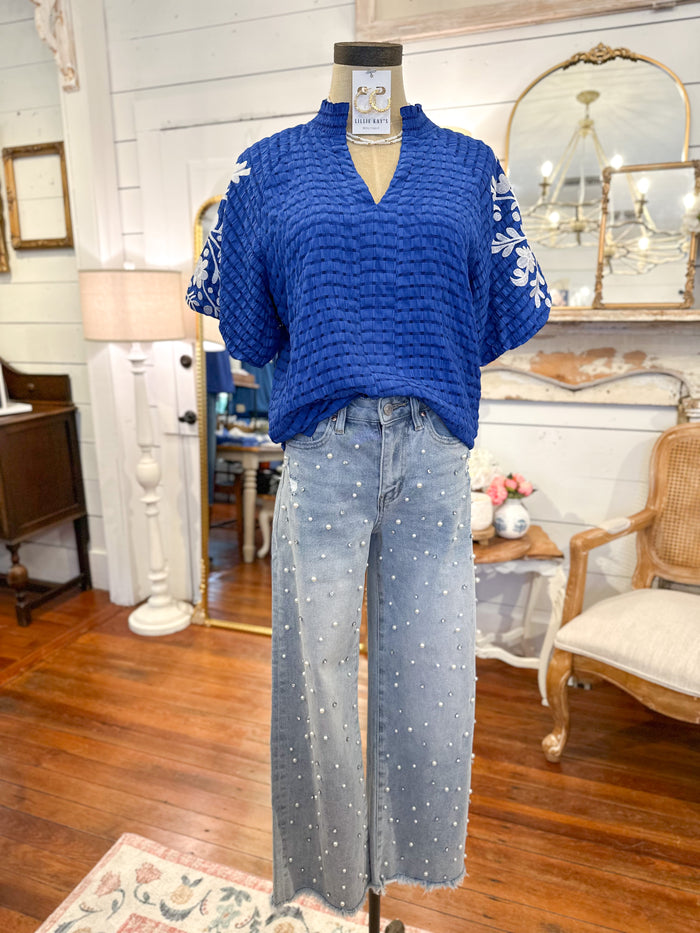 Mannequin wearing a blue textured top and light blue jeans in a room with wooden floor and furniture.