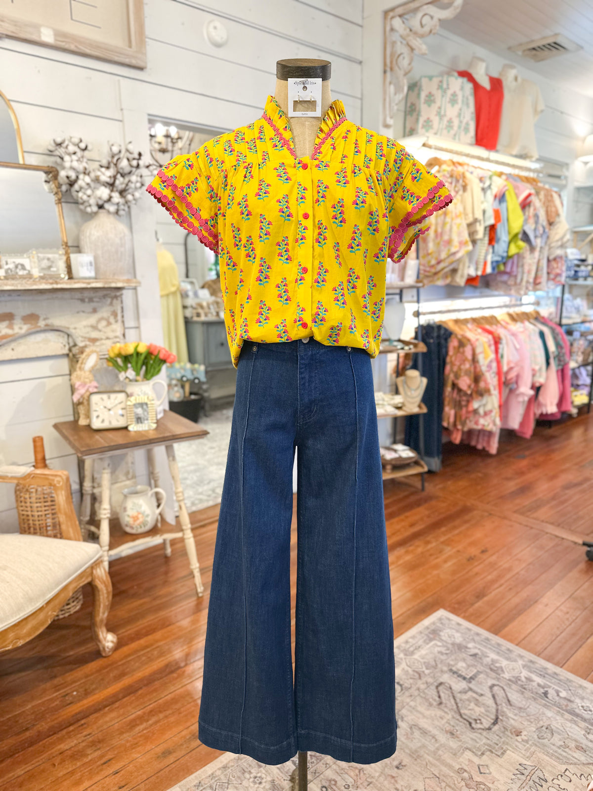 Mannequin wearing a yellow floral blouse and blue pants in a store setting