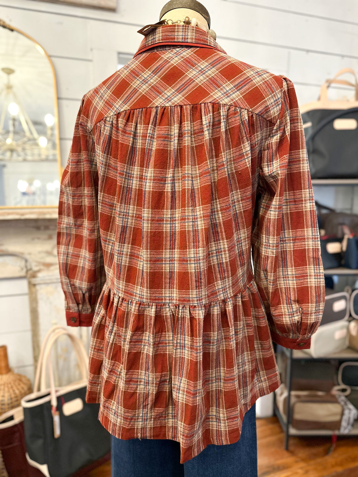 back of brick plaid button down blouse with ruffle hem on the back of top inside store setting 