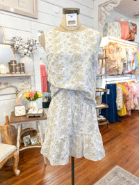 Floral embroidered skirt and top on a mannequin in a store setting with various items in the background.