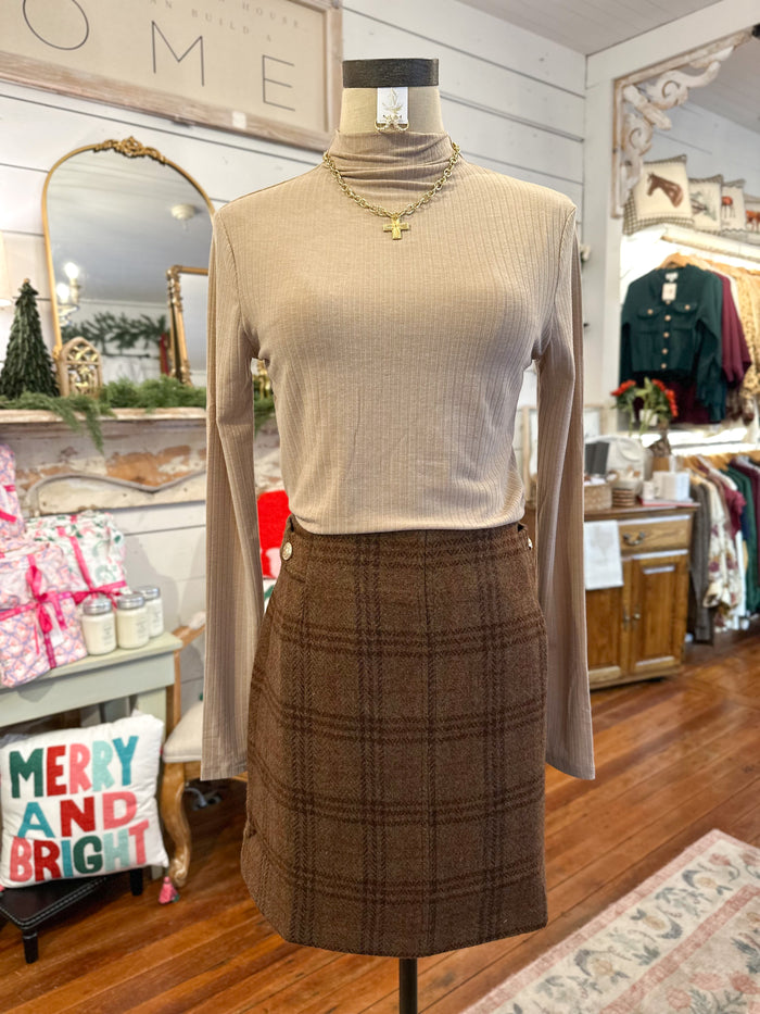 Mannequin wearing a beige long-sleeve top and brown plaid skirt in a store setting.