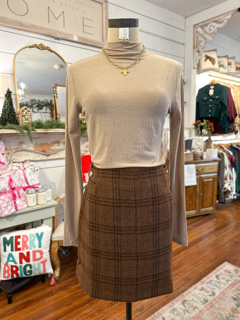 Mannequin wearing a beige long-sleeve top and brown plaid skirt in a store setting.