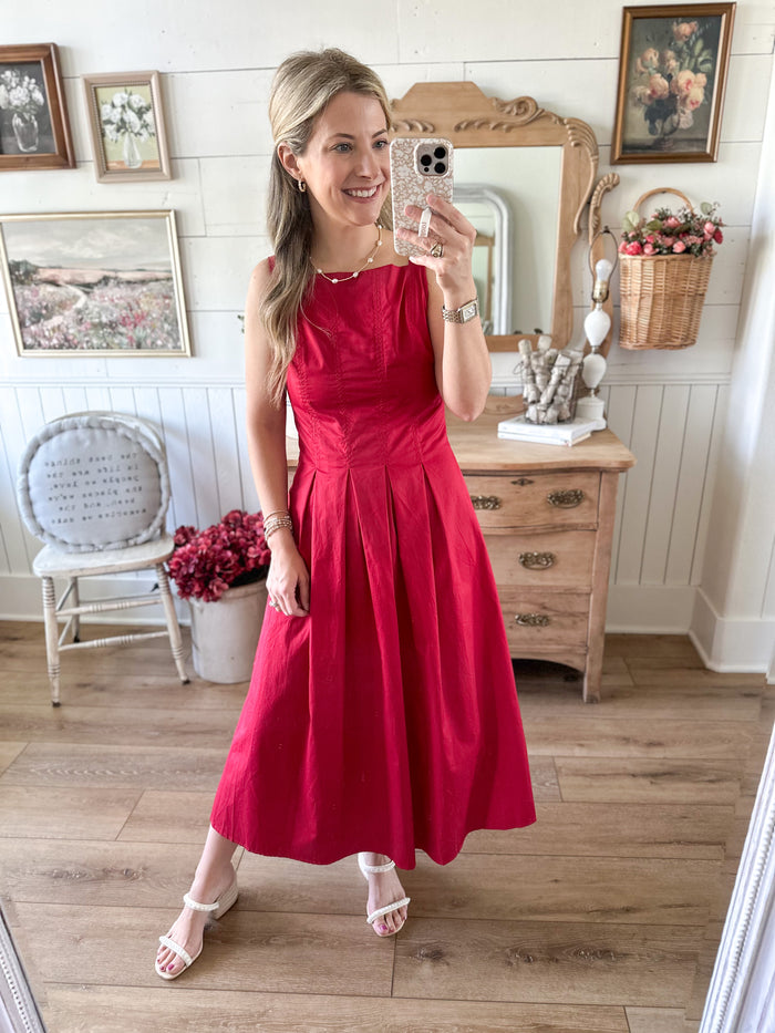 Woman in a red dress taking a mirror selfie in a room with wooden floor and framed pictures on the wall.