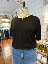 Mannequin wearing a black top and blue jeans with a necklace in a store setting.
