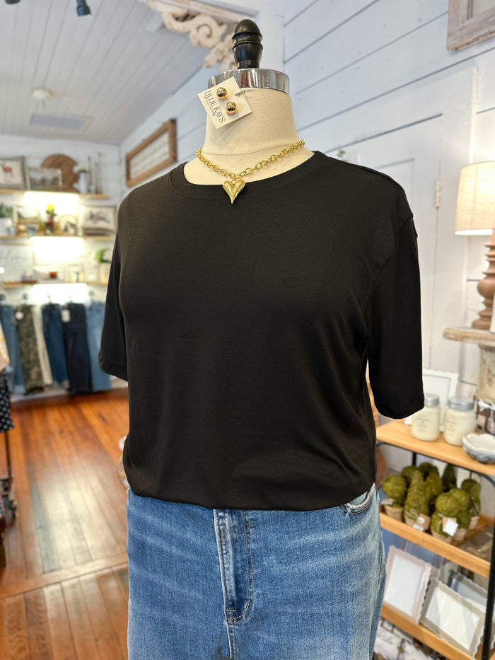 Mannequin wearing a black top and blue jeans with a necklace in a store setting.