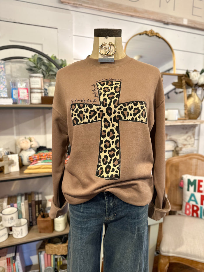 Mannequin wearing a brown sweatshirt with a leopard print cross design in a store setting.