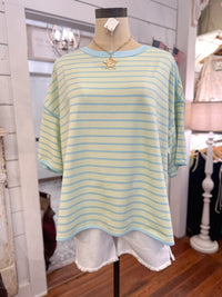 Mannequin wearing a green and blue striped shirt with a necklace in a store setting.