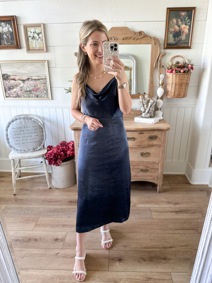 Woman in a blue dress taking a mirror selfie in a home setting.