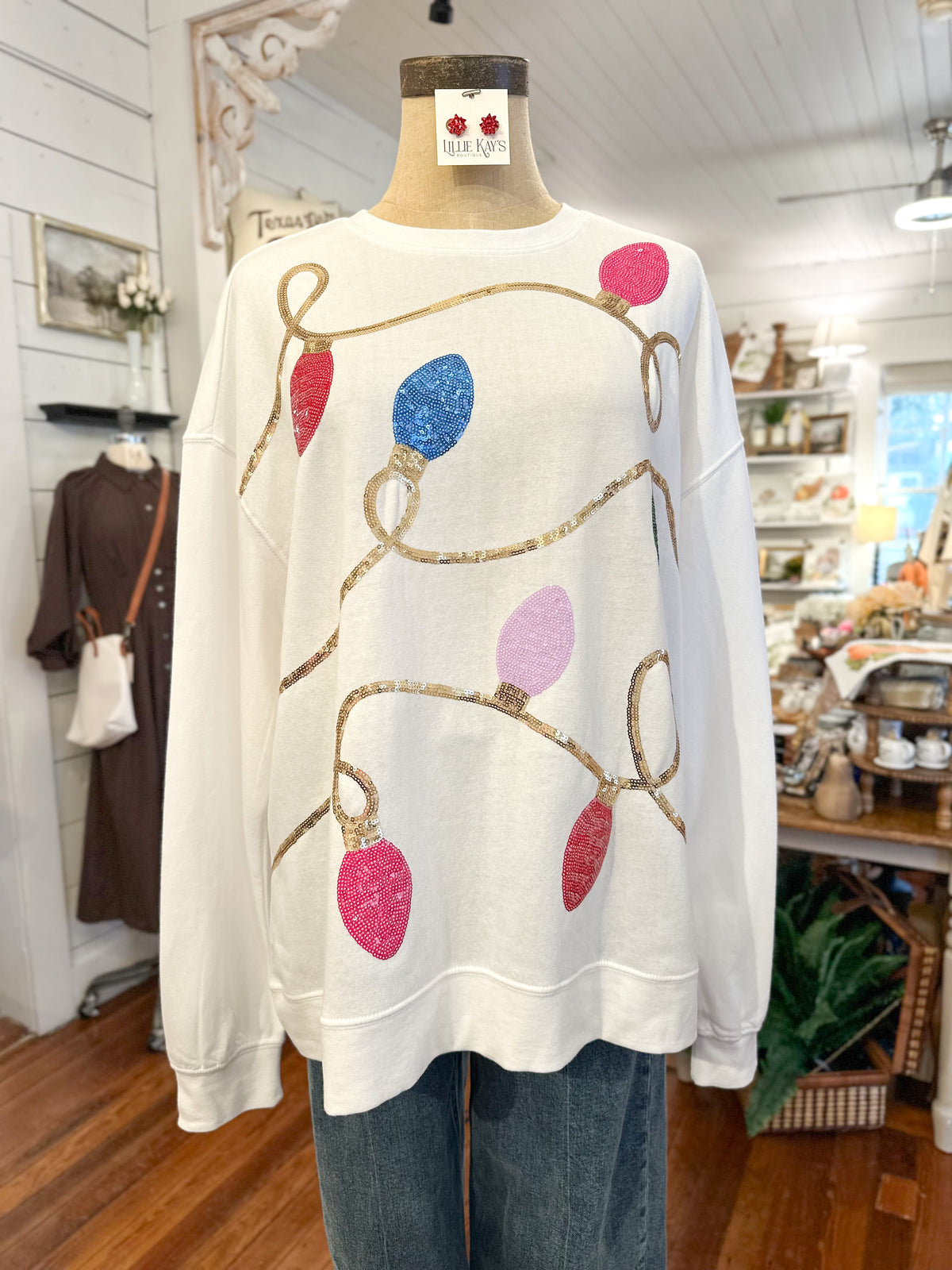 White sweater with colorful light bulb design on a mannequin in a store setting.