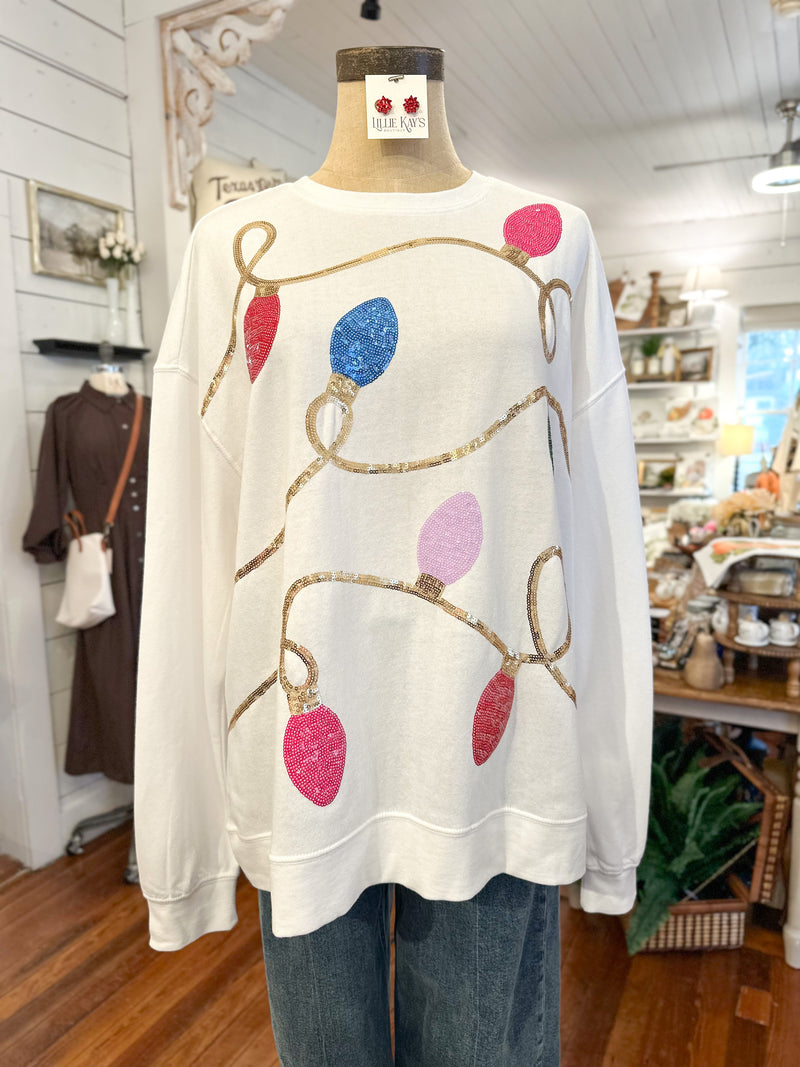 White sweater with colorful light bulb design on a mannequin in a store setting.