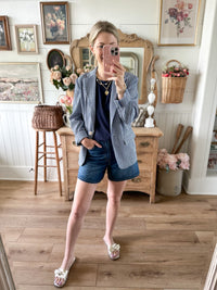 Woman taking a mirror selfie in a room with wooden floors and decorative elements. blue and white checkered blazer 