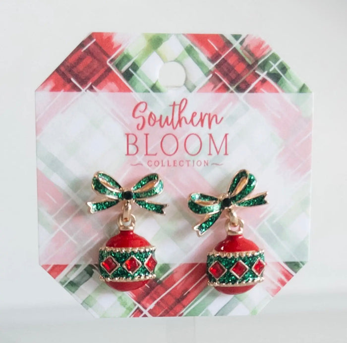A pair of Southern Bloom Collection holiday earrings featuring red and green ornament charms with glittery green bows, displayed on a festive plaid backing card.
