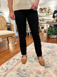 Person wearing black pants and brown shoes in a room with wooden floor and furniture.