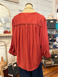 back of rust color umgee blouse inside store setting 