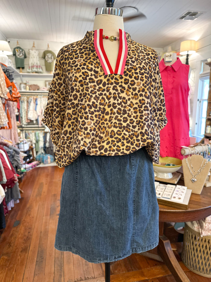 A leopard print blouse with a red and white striped collar, displayed on a mannequin in a clothing boutique alongside a blue denim skirt.