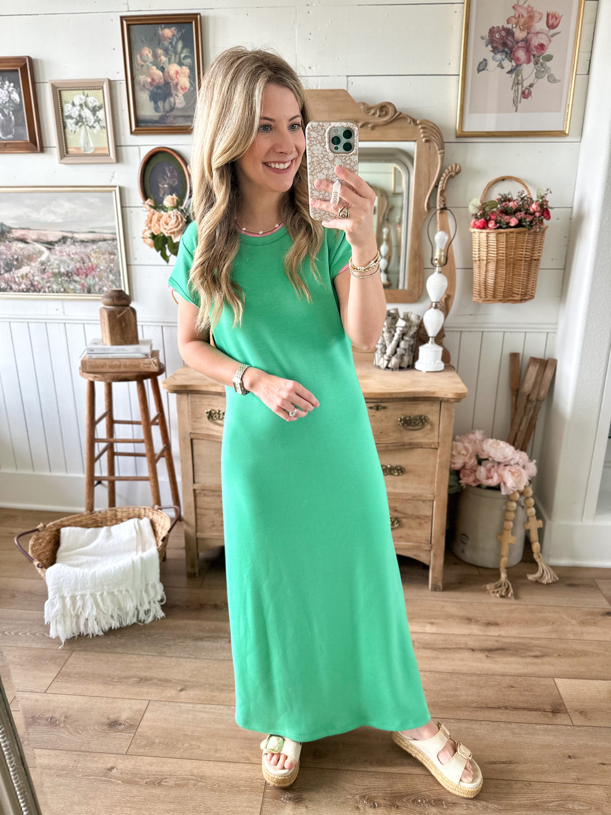 Woman in a green dress taking a selfie in a room with wooden furniture and decorative items.