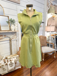 Green dress on a mannequin in a store setting with wooden floor and white walls.