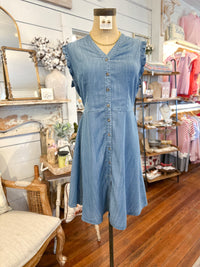 Blue denim dress on a mannequin in a store setting with wooden floor and shelves.